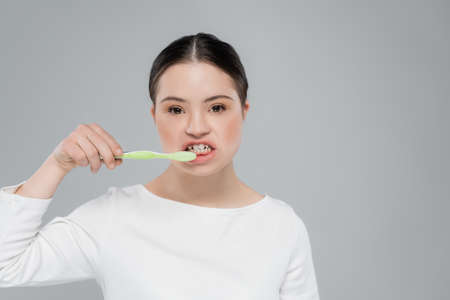 Woman with down syndrome brushing teeth isolated on greyの写真素材