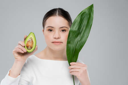 Woman with down syndrome holding leaf and avocado isolated on grey