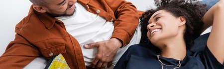 high angle view of cheerful african american couple looking at each other while resting on couch,...