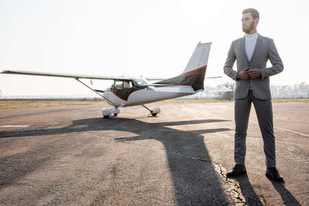 full length of bearded businessman in suit standing near helicopter outdoors