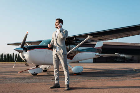 full length of cheerful businessman talking smartphone near helicopter outdoors