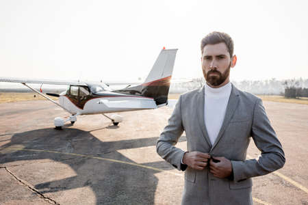 confident businessman adjusting blazer and standing near helicopter outdoorsの写真素材