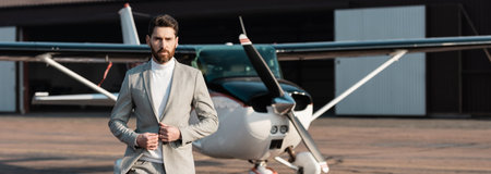 bearded businessman adjusting blazer and walking near modern helicopter outdoors, bannerの写真素材