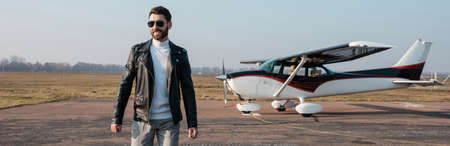 happy pilot in stylish leather jacket and sunglasses walking near helicopter, bannerの写真素材