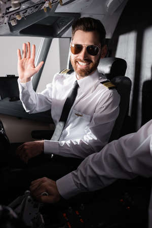 cheerful pilot in sunglasses waving hand near co-pilot in airplaneの写真素材