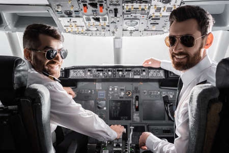 happy pilots in sunglasses and uniform looking at camera in airplane simulatorの写真素材