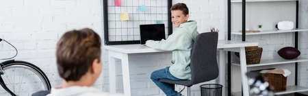 Smiling boy using laptop near blurred dad at home, bannerの写真素材