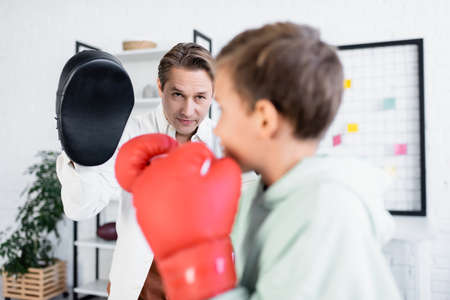 Dad in boxing pad looking at blurred son in gloves at home