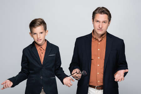 Serious father and boy in jackets looking at camera isolated on grey