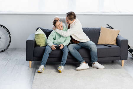 KYIV, UKRAINE - OCTOBER 11, 2021: Father touching son with joystick on couch at homeのeditorial素材