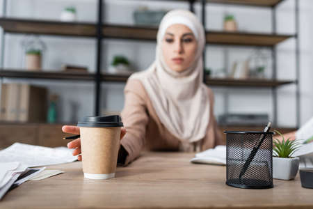 blurred arabian woman reaching paper cup while working at homeの写真素材