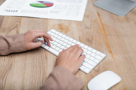 cropped view of woman typing on keyboard near computer mouse and graphs on deskの写真素材