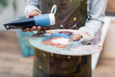 cropped view of blurred woman holding paint tube near palette