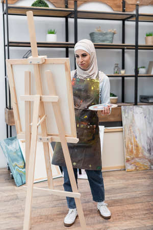 full length view of muslim woman painting on easel in home studioの写真素材