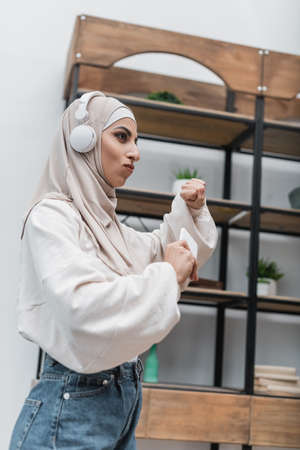 young muslim woman in headphones holding smartphone and dancing at homeの写真素材