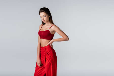 young model in red outfit posing with hand on hip isolated on gray
