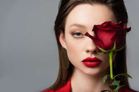 close up of young woman near red rose isolated on grayの写真素材