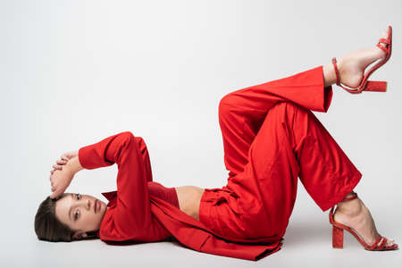 full length of trendy young woman in red suit lying on grayの写真素材