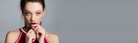 young woman holding necklace chain near red lips isolated on grey, banner
