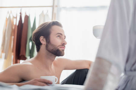 bearded man looking at woman in robe and holding cupの写真素材