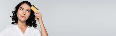 pensive young woman holding credit card with cashback isolated on grey, bannerの写真素材