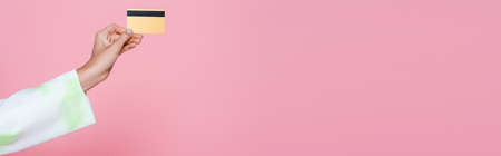 cropped view of young woman holding credit card isolated on pink, banner
