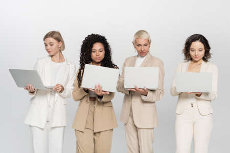 Multiethnic businesswomen using laptops isolated on grey, feminism conceptの写真素材