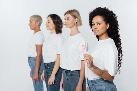 African american woman holding pink ribbon of breast cancer awareness near friends isolated on greyの写真素材