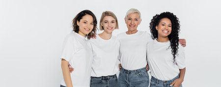 Cheerful interracial women hugging and looking at camera isolated on grey, bannerの写真素材