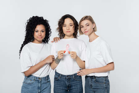 Interracial women hugging friend with ribbon of breast cancer awareness isolated on greyの写真素材