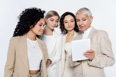 Senior businesswoman using digital tablet near interracial colleagues isolated on grey