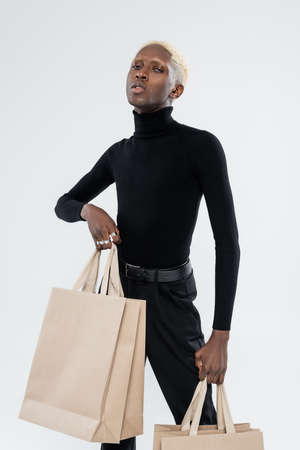 young african american man in totally black outfit holding shopping bags isolated on greyの写真素材