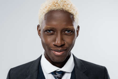 portrait of blonde and young african american man with blue eyes smiling isolated on greyの写真素材