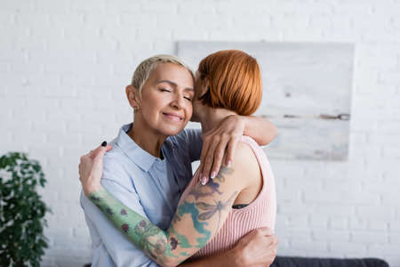 Lesbian woman with closed eyes hugging girlfriend at homeの写真素材