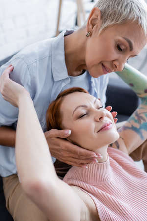 lesbian woman with closed eyes smiling near girlfriend touching her face at homeの写真素材