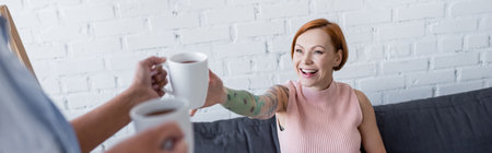 blurred woman holding tea cups near cheerful lesbian girlfriend, bannerの写真素材