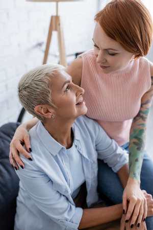 tattooed lesbian woman looking at happy girlfriend at homeの写真素材