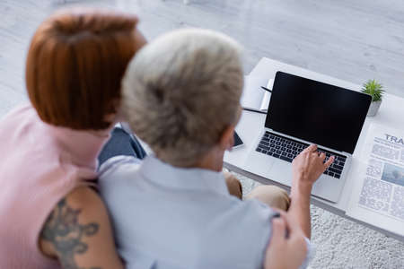 blurred woman hugging lesbian girlfriend using laptop with blank screen on coffee tableの写真素材