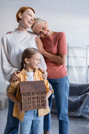 preteen girl holding house model near pleased same sex parents in new home
