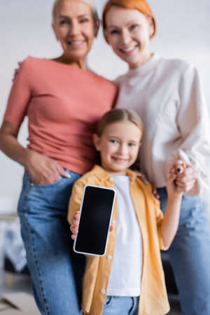 selective focus of smartphone with blank screen in hand of girl smiling near same sex parentsの写真素材