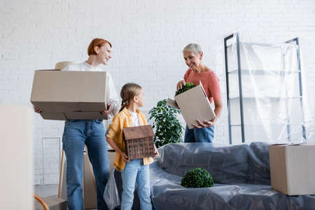 joyful lesbian women holding carton boxes near adopted girl with house model