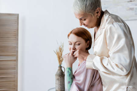 Lesbian woman in pajamas holding hand of girlfriend at homeの写真素材