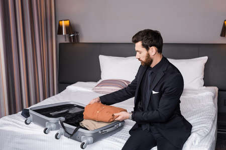 bearded man in suit unpacking baggage in hotel roomの写真素材