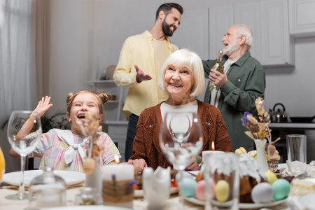 excited girl waving hand near smiling granny during festive dinner at homeの写真素材