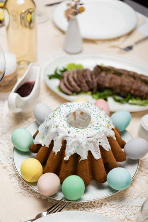 delicious easter cake with painted eggs near sauce and fried meat on blurred background