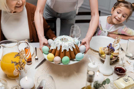 woman holding plate with painted eggs and easter cake near happy daughter and senior motherの写真素材