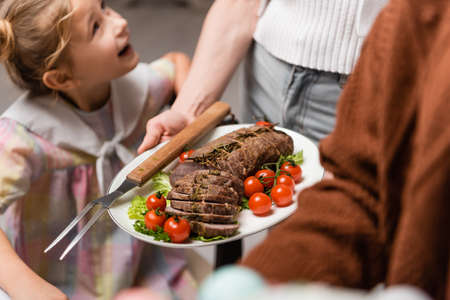 woman holding plate with meat and fresh vegetables near excited daughterの写真素材