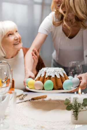 woman holding easter cake during festive dinner with senior mother