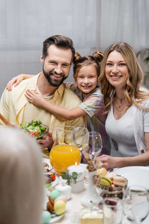 happy family looking at camera near table served with easter dinner
