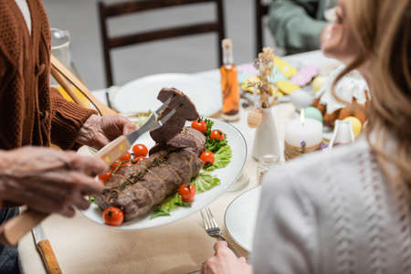 cropped view of senior woman serving meat near adult daughter during easter dinner
